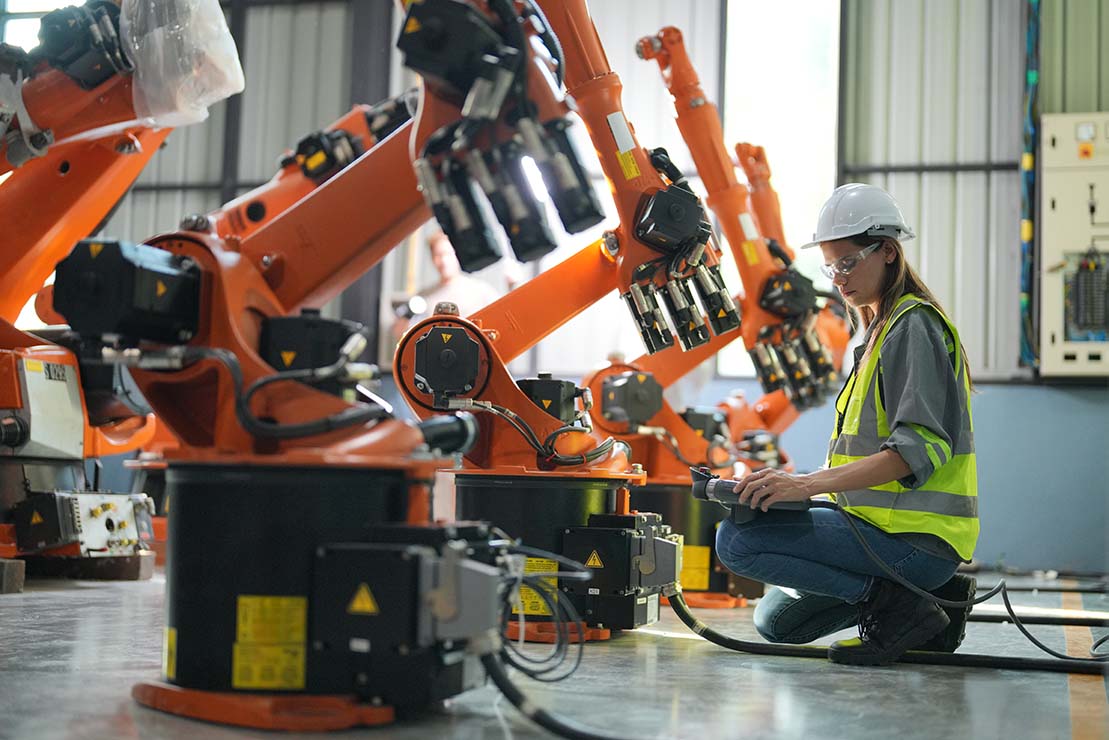Worker performing performance testing on orange robotic arms